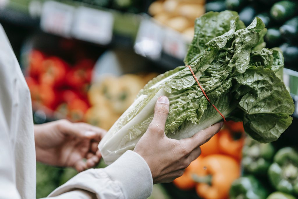 A person holding lettuce at a grocery store.