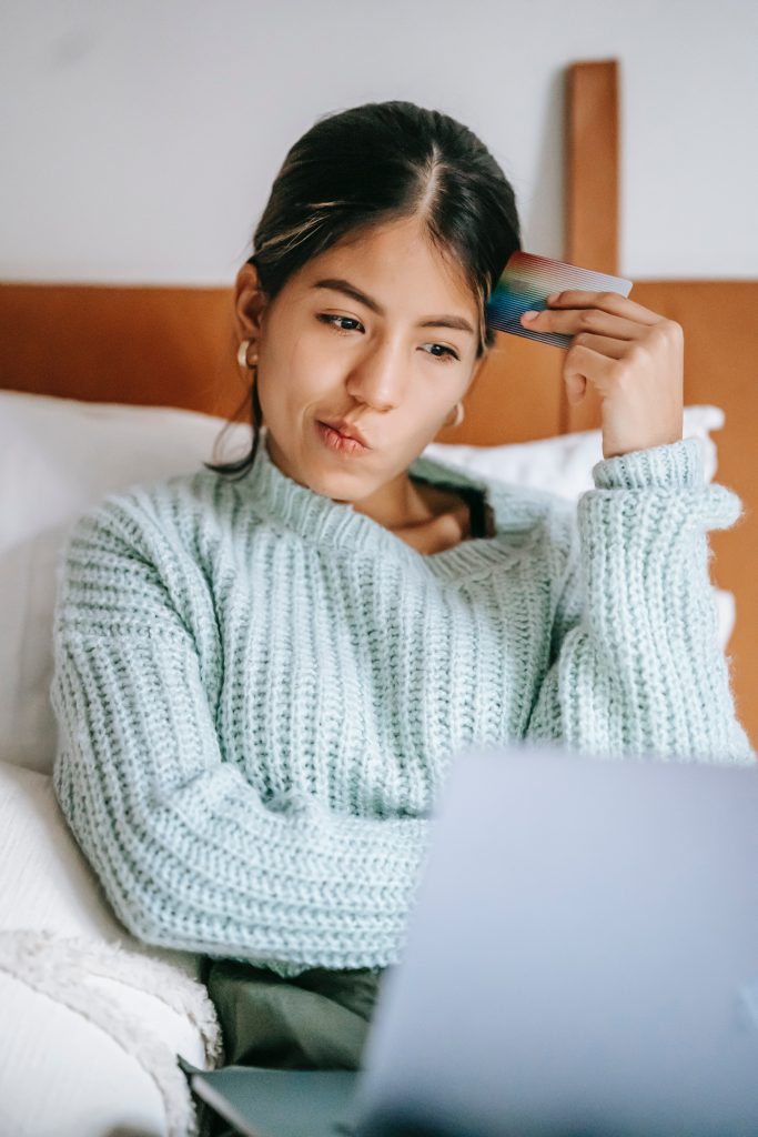 A young woman resting her head on the edge of her credit card while thinkikng.