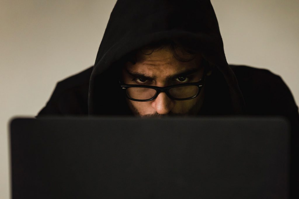 A man using a laptop. The man is hiding his face under a hood.
