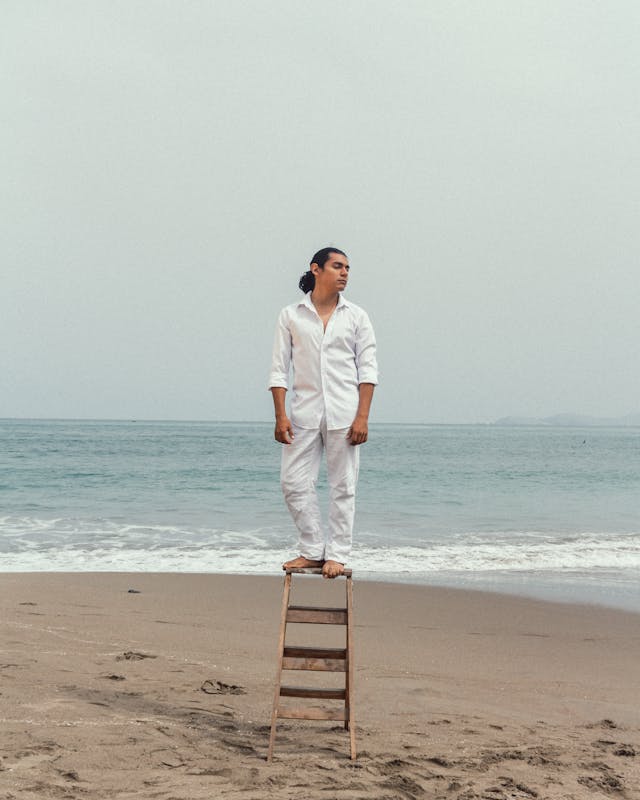 A person standing on a ladder on a sandy beach.