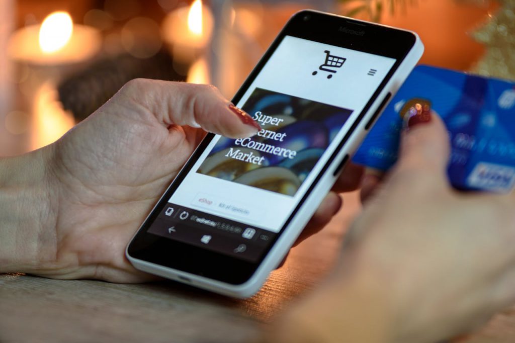 A person using their smartphone while holding a visa card in their other hand.