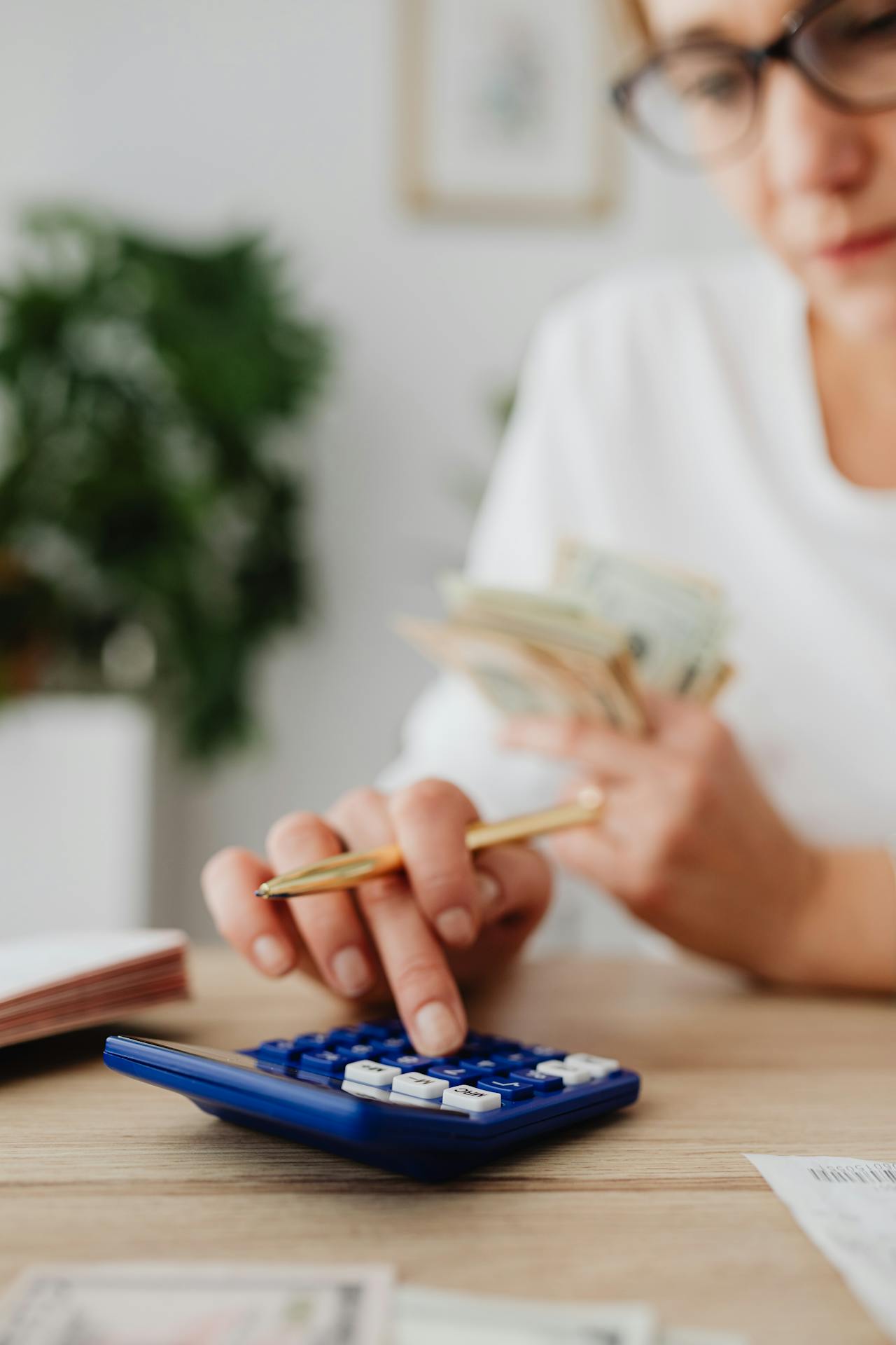 A woman holding cash while using a calculator.