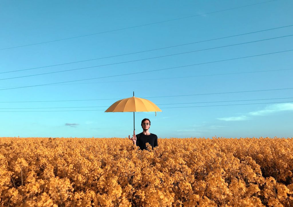 A man standing in an open field. He is holding an umbrella.
