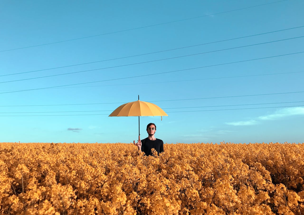 A man standing in an open field. He is holding an umbrella.