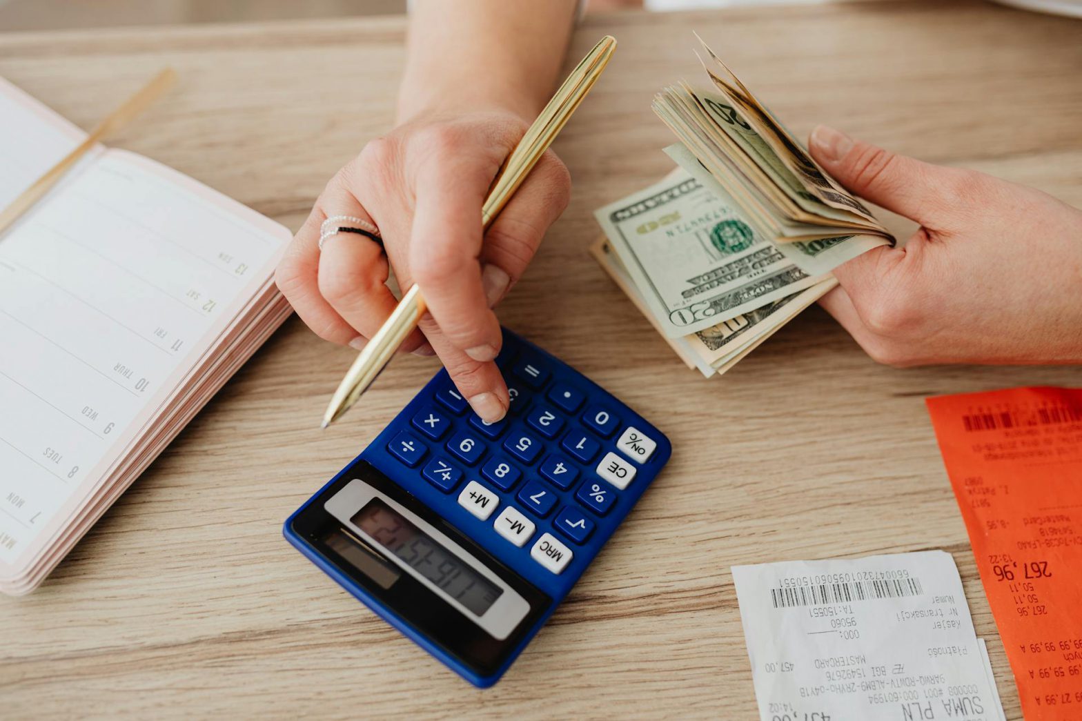 A person using a calculator and holding a stack of cash.